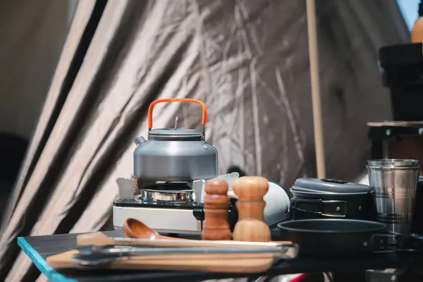 Campsite perfection, kettle, pot, pan, gas stove, flashlight, and camera neatly arranged at the front of the tent. Experience the joy of camping amidst natures beauty.