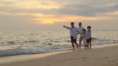 Baba, anne, çocuk dört çocuklu bir aile el ele yürüyorlar mutlu bir aile gün batımında kumlu bir sahilde koşuyor, tropikal yaz tatili