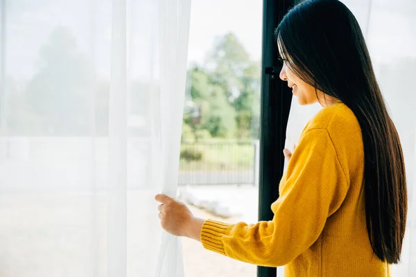Illustrating morning serenity, Woman opens curtains smiles at the view feeling refreshed and relaxed at home. Embracing joy relaxation and a cheerful start to the day.
