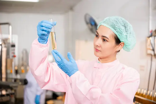 A woman food engineer in juice beverage factory executes food and beverage quality and safety testing employing test tubes to sample basil or chia seeds in bottled products in laboratory control.