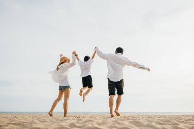 Aile içi açık hava aktiviteleri, aile içi anne-baba ve oğul şafak vakti el ele tutuşup havaya atlamak mutlu Asyalı aile bireyleri yaz tatili seyahatlerinde sahilde birlikte eğleniyor.