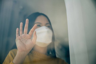 Tıbbi maske takan bir kadın, salgın sırasında COVID-19 'un önlenmesini ve ev karantinası kavramını vurgulayarak evde kendini izole ediyor..
