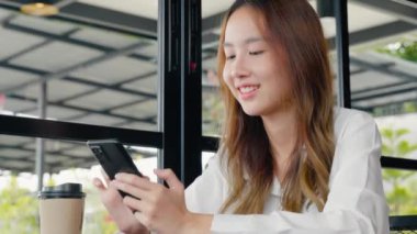 Güzel bir Asyalı kadın havale yapıyor. Finansal internet bankacılığı cep telefonunda. Genç bir kadın sabahları pencerelerin yanındaki kafede online alışveriş yapmak için akıllı telefon kullanıyor.