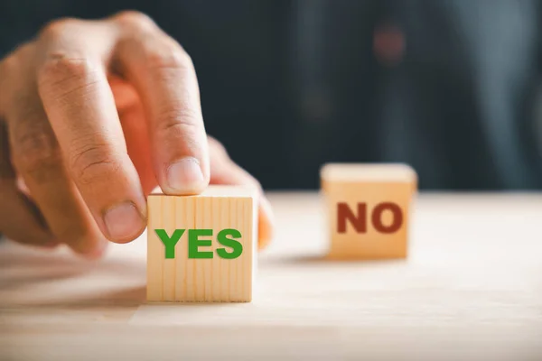 Hand of businessman selects between two wooden cubes marking check for right and wrong choices. Communication of choice and validation presented. Think With Yes Or No Choice.