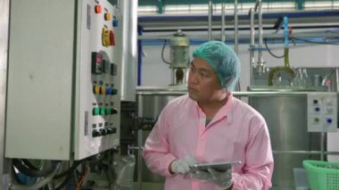 Bir içecek fabrikasında, bir mühendis makineleri izlerken, tablet kullanan bir işçi soda doldurma işlemini denetler. Kalite kontrolünün vurgulanması şişe imalatında yüksek standartları güvence altına alır.