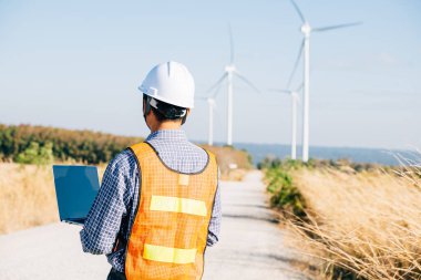 Dizüstü bilgisayarı rüzgar türbinleriyle çalışan bir mühendis. Servis teknisyeni türbin verimliliğini sağlıyor. Peyzaj geliştirme için yenilik yel değirmeni kalitesi ve hizmeti için güvenilir bir şekilde çalışıyor.