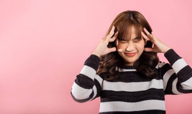 Portrait of beautiful Asian young woman sad tired strain face holding hold head by hands, stress female person unhappy closed eyes problem she headache, studio shot isolated on pink background