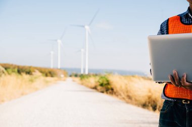 Yel değirmenlerindeki bilgisayarlı adam. Mühendis türbin verimliliğini sağlıyor. Hizmet teknisyeni, kaliteyi ve yeniliği vurgulayan manzara geliştirme üzerinde kendinden emin bir şekilde çalışıyor.