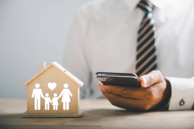 Aile refahını ve güvenliğini sağlamak. Odunlukta aile silueti olan cep telefonu tutan bir iş adamı. Aile, yaşam, sağlık ve ev sigortası ikonları. Sigorta konseptini yansıtmak.