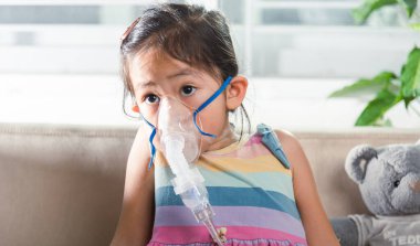 Kid girl making makes inhalation nebulizer steam sick cough at home, Asian Child using nebulizer mask equipment alone have smoke, stuffy nose and runny, oxygen spray inhaler therapy, Health medical