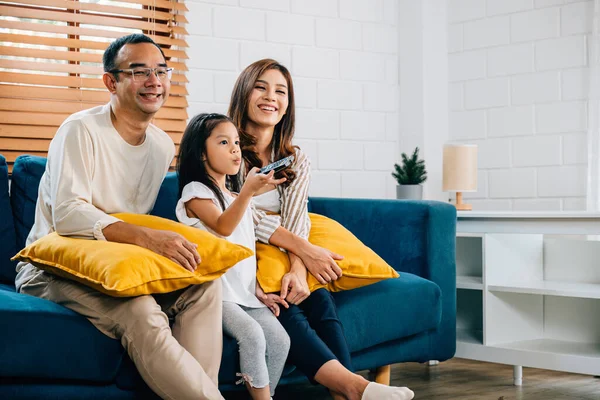 An Asian family is joyfully bonding watching TV at home on the sofa. The father mother son and daughter share togetherness relaxation and happiness during their weekend time.