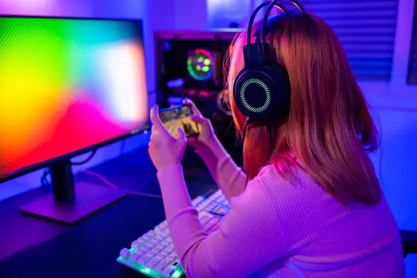 Asian woman live stream she play video game via smartphone at home neon lights living room, Gamer playing online game application on mobile phone wear gaming headphones, E-Sport concept