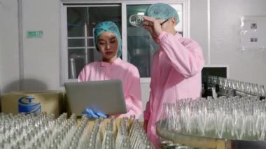 Bir içecek fabrikası hattında iki mühendis taşıma bandındaki ürün şişelerini denetliyor. Detaylı analiz için dizüstü bilgisayar kullanan yetenekli profesyoneller tarafından yürütülen kalite kontrol ve teftiş.