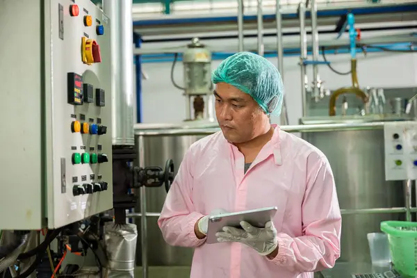 In a beverages factory a worker using a tablet oversees soda water filling while an engineer monitors machinery. Emphasizing quality control ensures high standards in bottle manufacturing.