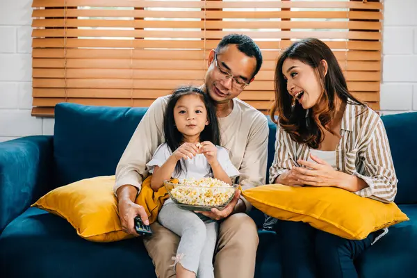 Modern family shares happiness and togetherness in living room watching a video with popcorn. father mother son daughter and schoolgirl create precious family moments filled with smiles and laughter.