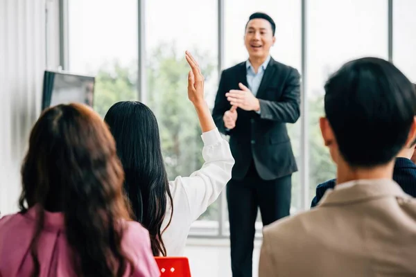 During a conference, a diverse crowd of businesspeople raises their hands to ask questions, vote, or volunteer. This scene emphasizes teamwork and active audience involvement.