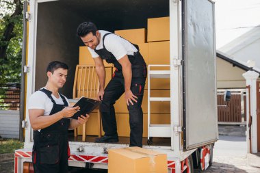 Üniformalı Mover çalışanları kutuları boşaltıp listeyi kontrol ediyorlar. Profesyonel teslimat servisi sorunsuz bir yer değiştirme ve verimli bir nakliye sağlıyor. Taşınma günü konsepti