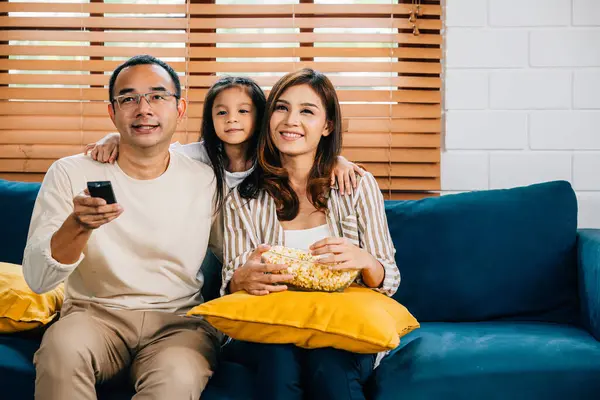 In warm atmosphere of their house smiling young family bonds while watching TV with popcorn. father mother son daughter and schoolgirl radiate happiness epitomizing togetherness and candid enjoyment.