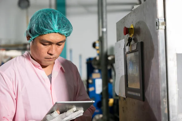 In beverage manufacturing a worker with a tablet supervises soda water filling while an engineer inspects machinery. Quality control ensures top-notch bottle production standards.