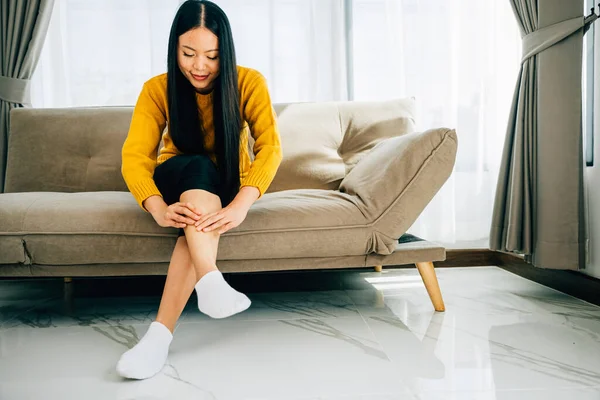 Highlighting health care concept, woman on sofa holds her injured ankle. Emphasizing varicose vein prevention leg recovery and pain relief for the patient. medical