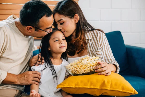 In their comfortable living room family enjoys quality time watching TV with popcorn. father mother daughter and sibling are all smiles fostering togetherness and happiness.