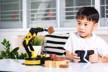 Happy Asian little boy using remote control playing robotic machine arm for pick up wood block, Funny learning successful getting a lesson control robot arm, Technology science education concept