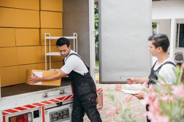 Üniformalı, gülümseyen nakliye şirketi çalışanları yeni bir eve taşınmak için kamyondan kutuları etkili bir şekilde boşaltıyor. Takım çalışması ve yer değiştirme servisi mutluluk getirir. Taşınma Günü