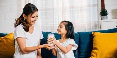 Asyalı bir annenin kızına kanepede bir bardak süt ikram etmesi harika bir aile anıydı. Bu resim mutluluk masumiyeti ve kalsiyumun besin değeri yayıyor..