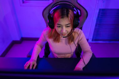 Young player woman wearing gaming headphones intend to do playing live stream games online at home, Happy Gamer endeavor plays online video games tournament with computer desktop with neon lights