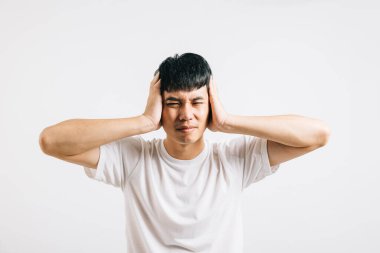 Acı çeken bir adam, çaresizce elleriyle kulaklarını kapatıyor ve bağrışma sesinden kaçmak için gözlerini kapatıyor. Stüdyo çekimi beyaza izole edilmiş, sıkıntısını gösteriyor..