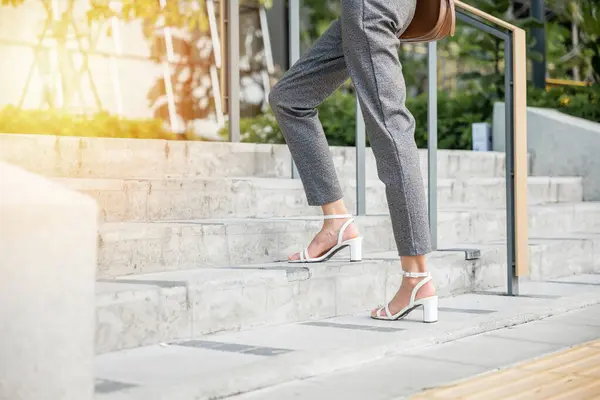 Businesswoman in modern suit is captured in moment of ambition climbing city stairs. Her black shoe-clad foot symbolizes relentless effort and progress embodying spirit of success in corporate world.