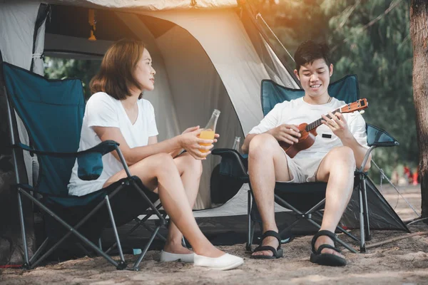 Love-filled moments at the campsite, An Asian couple playing the ukulele and singing, surrounded by the warmth of their tent. Their smiles reveal the joy of togetherness. Happiness is in the air.