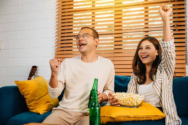 A jubilant Asian couple husband and wife cheer for a football goal during their leisure weekend creating an atmosphere of joy excitement and togetherness as dedicated sports enthusiasts.