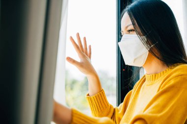 Tıbbi maskeli genç bir kadın, Coronavirus salgını sırasında ev karantinası ve COVID-19 önlemesini vurgulayarak kendini karantinaya aldığı için evde izole ediyor..