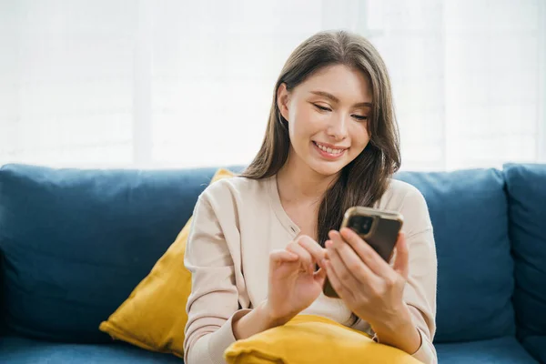 Amid home comfort a woman on a sofa types a message on her phone embracing successful communication. With a smiling face she enjoys technology and relaxation. The woman is relaxing.