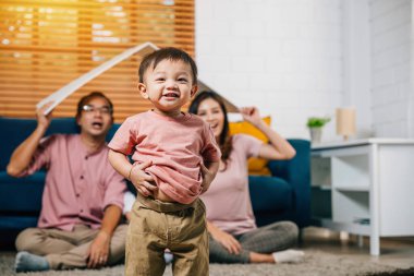 Konut ve yer değiştirme kavramında karton çatılı sevecen bir aile yeni evlerindeki bir kanepede toplanıyor. Güvenlik mutluluğu ve aile desteği bu mutlu anın özüdür..