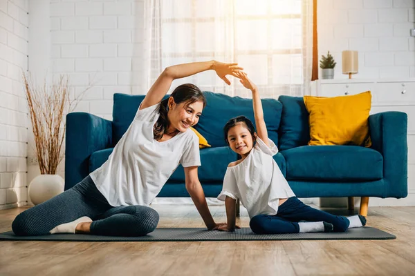 A mother coaches her little daughter in yoga creating a family bond filled with happiness relaxation and togetherness. Their smiles reflect joy and vitality in their domestic life.