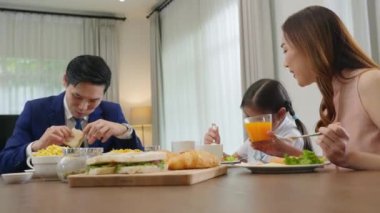 Asian family father, mother with children daughter eating healthy breakfast food on dining table kitchen in mornings together at home before father left for work, happy couple adult family concept