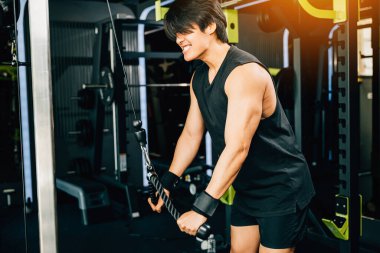 Kablolu trisepsleri çeken genç bir yetişkin, kaslarını ve pazılarını şekillendirmek için bir çekme makinesi kullanıyor. Üst vücut kuvveti egzersizi.