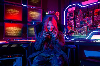 Asian woman live stream she play video game via smartphone at home neon lights living room, Gamer playing online game application on mobile phone wear gaming headphones, E-Sport concept