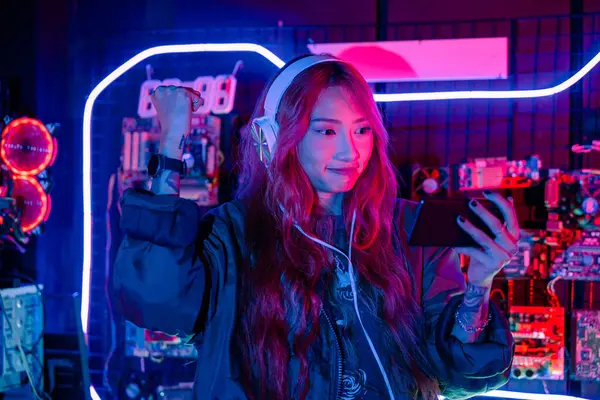 Kazanmak. Oyun odasında heyecanlı hisseden kafası karışmış Asyalı kadın, neon ışıklı akıllı cep telefonuyla video oyunu oynayan Happy Gamer, kutlama yapmak için elini kaldırıyor.