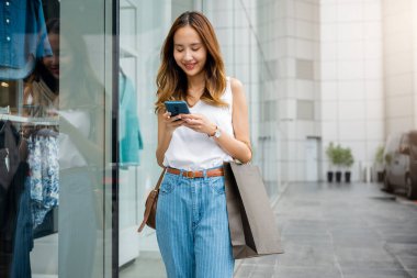 Siyah ceketli bir kadın telefon ekranına gülümsüyor, mesajlaşırken ve mesajlaşırken kaybolmuş. Modern teknolojinin ve kablosuz bağlantının keyfini çıkarıyor..