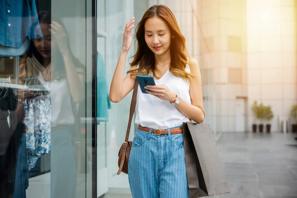 若い女性が街の壁に向かって立っている間 スマートフォンをスクロール 彼女の携帯電話は ソーシャルメディアとエンターテイメントの仮想世界への彼女の窓です — ストック写真