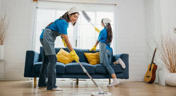 厄介なリビングルームでは 制服を着た女性2人が従業員を掃除しています 手袋を施して 家具のソファーや床にほこりや汚れを取り付ける ルーチンは 家事と衛生です 中小企業 — ストック写真