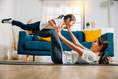 Uyumlu bir aile evde yoga yaparken küçük kuş duruşu yapıyor. Annelerin desteği ve kızların neşesi güven mutluluk ve birliktelikle dolu neşeli ve uyumlu bir an yaratır..