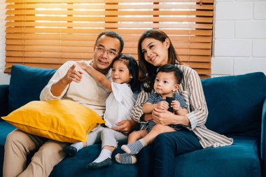 Evde televizyon izlerken modern bir kanepede neşe dolu genç bir aile. Baba, anne, kardeş, birlikte ve mutluluk saçan değerli aile zamanlarını paylaşıyor..