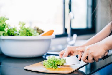 Mavi önlüklü bir kadın yakın plan çekimde sağlıklı bir salata için taze sebze keser. Evde bir aile yemeği için besleyici malzemeler hazırlamak..