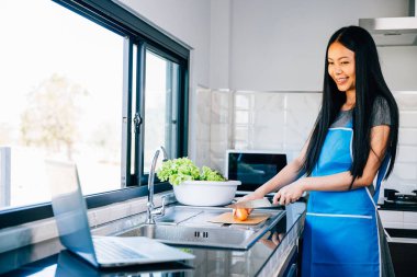 Bir kadın dizüstü bilgisayarında yemek tarifi aramaktan zevk alır. Yemek hazırlama ve aşçılık çalışmalarında teknolojinin neşe ve rahatlığını yansıtıyor..