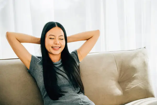 Relaxed woman on sofa hands behind head enjoys serene moment. Dreaming finding balance in modern living room. Embracing relaxation wellbeing and mindfulness at home. Kick back and relax concept