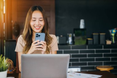 Dizüstü bilgisayarla çalışan mutlu bir iş kadını Cefa 'da cep telefonuyla mesaj atıyor. Kahve dükkanında akıllı telefon kullanarak gülümseyen genç bir kadın.